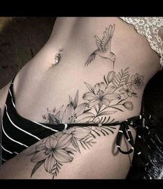 a woman's stomach with flowers and a bird tattoo on her side ribcage