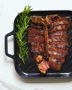 a steak on a grill with rosemary garnish in the foreground and another piece of meat sitting on top of it