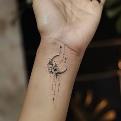 a woman's arm with a small tattoo on the wrist and stars hanging from it