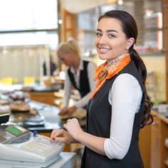 a woman standing in front of a cash register machine at a counter with people behind her