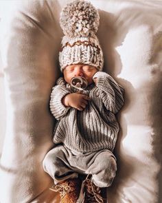 a baby wearing a knitted hat and sweater is sleeping on a pillow with a bottle in it's mouth