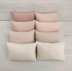 six pillows stacked on top of each other in different colors and sizes, all lined up against a white wooden wall