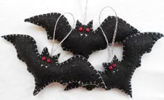 three black bats with red eyes hanging on a white cloth covered wall ornament