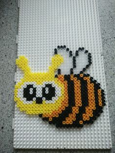 a beaded picture of a yellow and black bee on a white mat with grey background