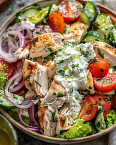 a salad with chicken, tomatoes, cucumbers and dressing in a bowl on a table