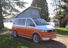 an orange and white van parked in front of a lake