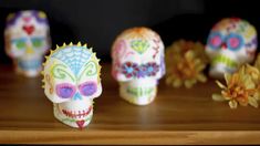 three skulls with different colors and designs on them sitting on a table next to flowers