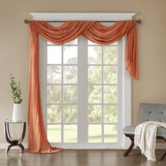 a living room with a chair and window covered in curtained drapes on the windowsill