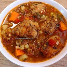 a white bowl filled with meat and vegetable soup on top of a wooden table next to a spoon