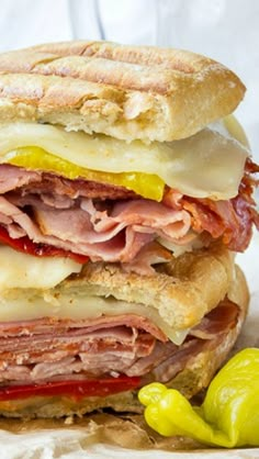 a close up of a sandwich with meat, cheese and peppers next to a pickle