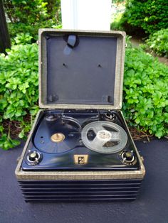 an old fashioned record player sitting on top of a table next to some bushes and shrubbery