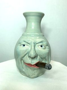 a green face vase with a pipe sticking out of it's mouth on a white surface