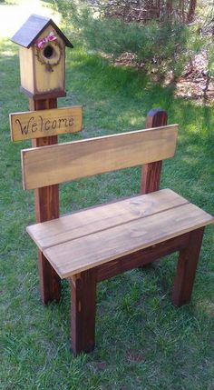 a wooden bench sitting in the grass next to a birdhouse and sign that says welcome