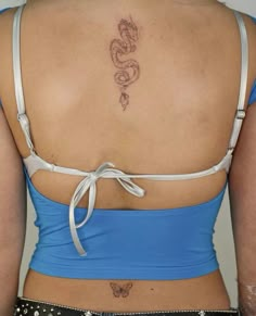 the back of a woman's blue top with a dragon tattoo on her left side