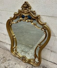 an ornate gold framed mirror against a white brick wall