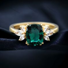 an emerald and white diamond ring on a black cloth