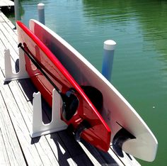 a red and white surfboard sitting on top of a wooden dock next to water