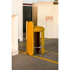 a yellow stool sitting on top of a floor next to a wooden table and chair