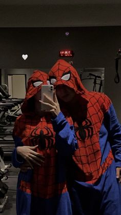 two people in spider man costumes are taking a selfie with their cell phone at the gym