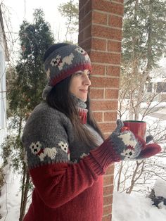 a woman holding a cup in her hand while standing next to a brick building with snow on the ground