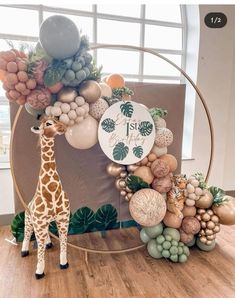 a giraffe standing in front of a circular display with balloons and greenery