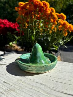 a green glass bowl sitting on top of a wooden table next to some orange flowers