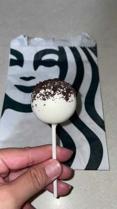 a hand holding a chocolate covered lollipop on top of a white and black napkin