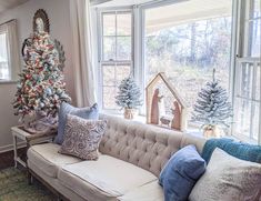 a living room filled with furniture and a christmas tree in the window sill next to a couch