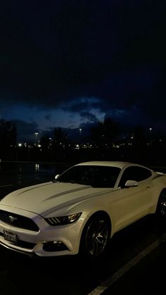 a white car parked in a parking lot next to a body of water at night