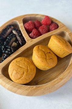 three muffins and raspberries in a wooden tray on a white surface