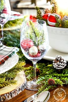 a christmas table setting with pine cones, evergreen branches and other holiday decorations on the table