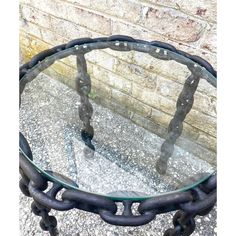 a glass and metal table with chains on the bottom, sitting in front of a brick wall