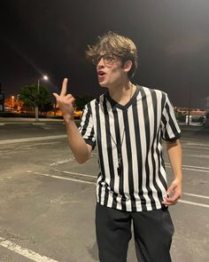 a man standing in an empty parking lot with his hand up to the side while wearing a referee's uniform