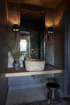 a bathroom sink sitting under a mirror next to a potted plant and two lights