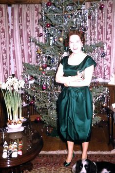 a woman standing in front of a christmas tree next to a black and white dog