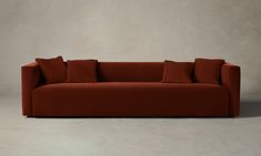 a red couch sitting on top of a white floor next to a wall with two pillows