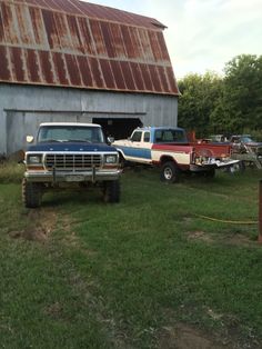 two pickup trucks parked in front of a barn with rusted tin roof on it