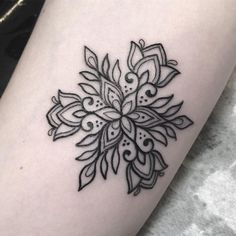 a black and white tattoo design on the thigh, with an intricate flower in the center