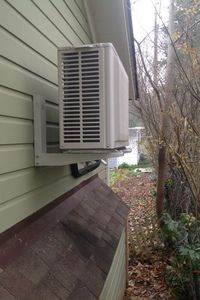 an air conditioner mounted on the side of a house next to a tree and bushes