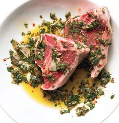 two pieces of meat on a white plate covered in herbs and seasoning sprinkles