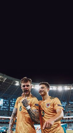 two men standing next to each other in front of a soccer field with the lights on