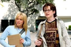 a young man and woman standing next to each other in front of a building with trees