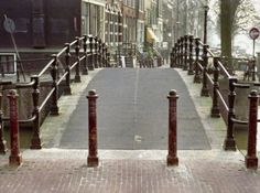 an empty sidewalk with railings and street signs on either side, in front of some buildings