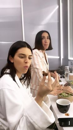 three women sitting at a table with food in front of them and one woman standing behind her