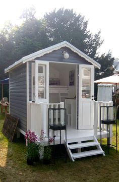 a small white and gray house with steps leading up to the front door on grass