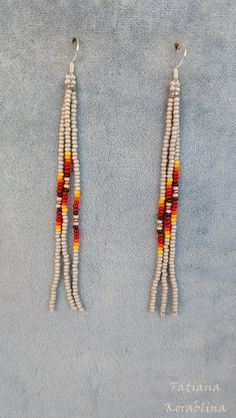 two pairs of beaded earrings on a blue surface with white and red beads hanging from them