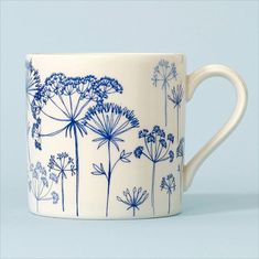 a blue and white coffee cup with dandelions printed on the outside, sitting on a light blue surface