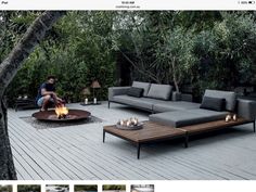 a man sitting on top of a couch next to a fire pit in the middle of a wooden deck