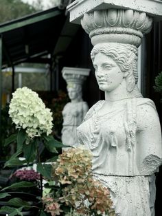 there is a statue next to flowers in the bushes and on the ground, with one woman's head resting on a planter