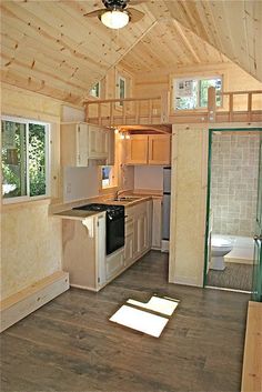 an empty kitchen and living room in a tiny cabin with wood flooring, windows, and ceiling fan